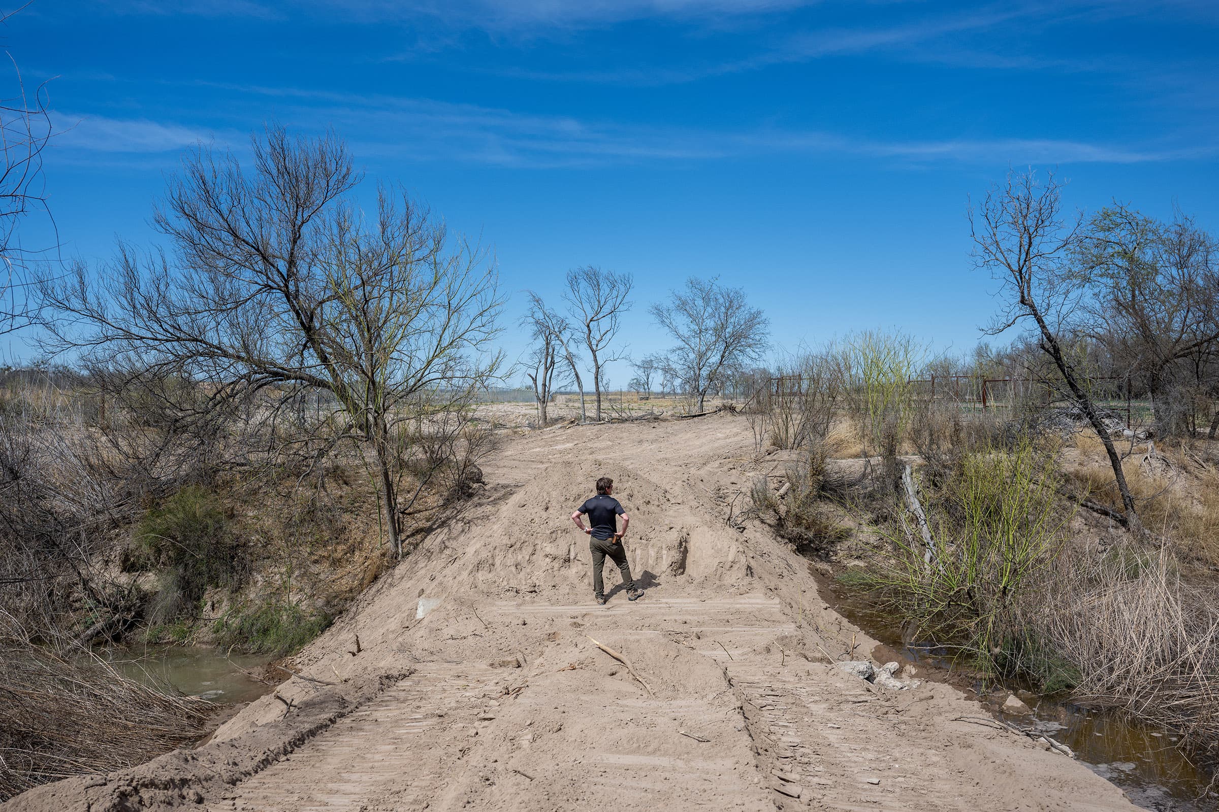 A man surveys water flow from a dusty road.