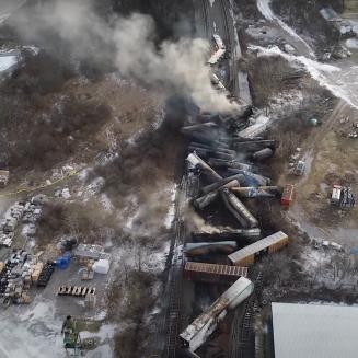 Train cars scattered and crush following a derailment, with smoke coming from the accident scene.