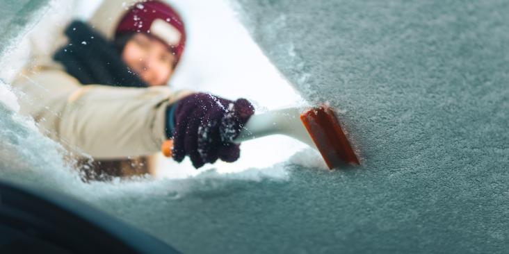 Woman cleans windshield with ice scraper