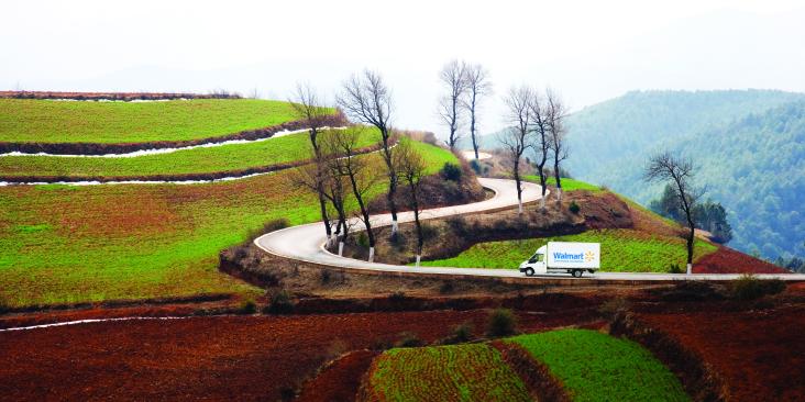 Walmart truck drives up a curved road in a scenic landscape.