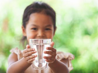 A little girl holds up a glass of drinking water.