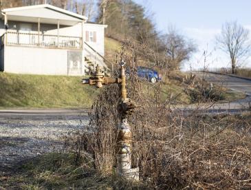 A rusty pipe sticking out of the ground with a house and car in the near background.
