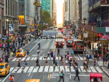 People crossing at a crosswalk in a bit of timelapse blur on a sunny New York City street.
